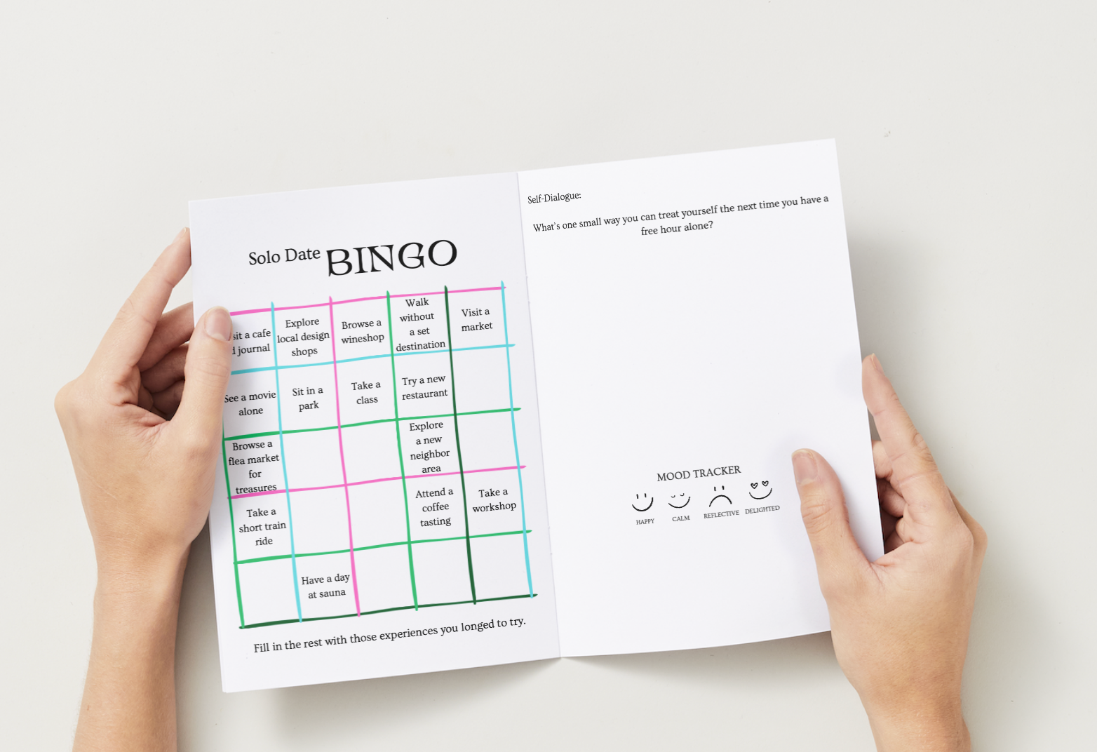 Person holding a book with a Solo Date Bingo sheet on a white background