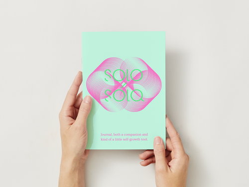 Hands holding a green journal with pink design and text on a light gray background